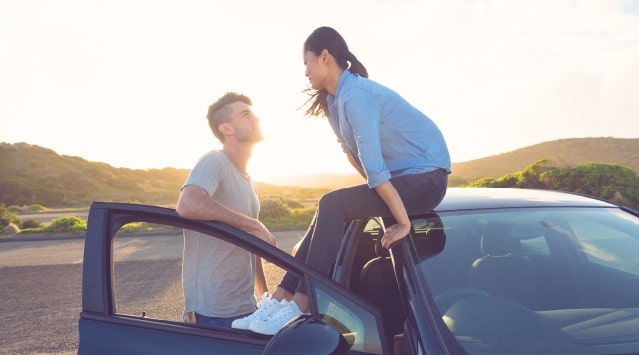 A Man Talking to a Woman Sitting on a Car